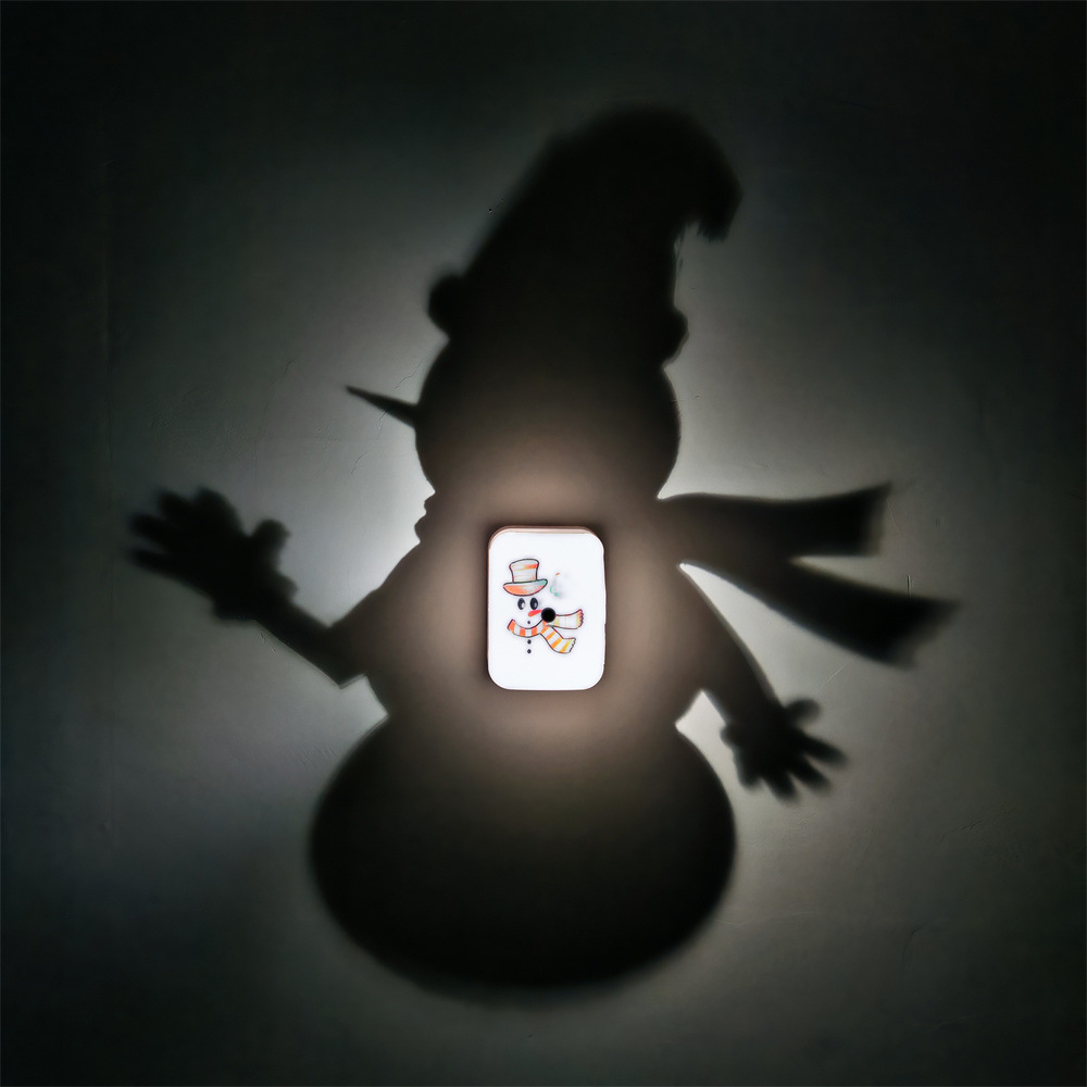 Christmas Snowman Shadow Lamp with an illuminated snowman scarf illustration casting an oversized winter hat snowman silhouette on a wall