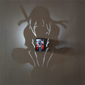 Itachi-inspired anime shadow projection lamp showing a long-haired crouching ninja wall silhouette and a red and black Akatsuki-inspired illustration centerpiece