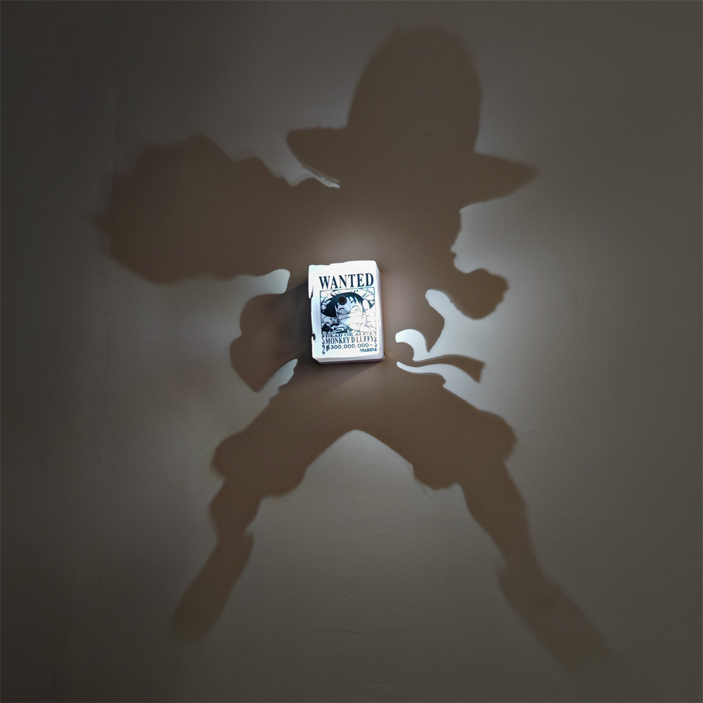 Luffy-inspired anime shadow projection lamp creating a large straw-hat silhouette on a wall with a WANTED poster centerpiece
