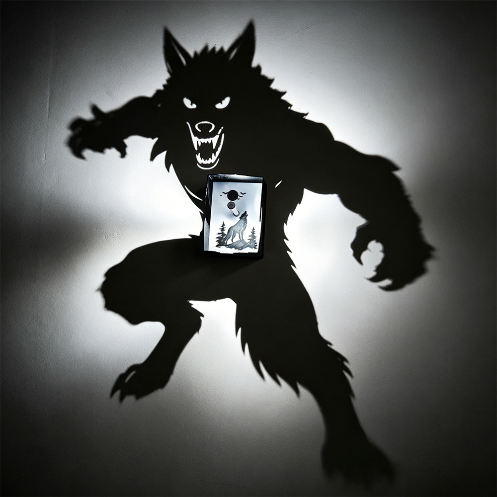 Werewolf moonlight shadow projection lamp casts oversized snarling beast silhouette with fangs and claws while showing a howling wolf illustration on its center panel